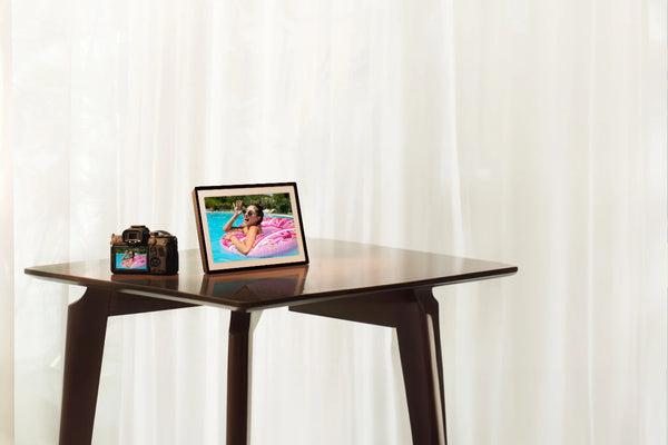 Table with a tablet displaying a beach scene and a camera on a white curtain background