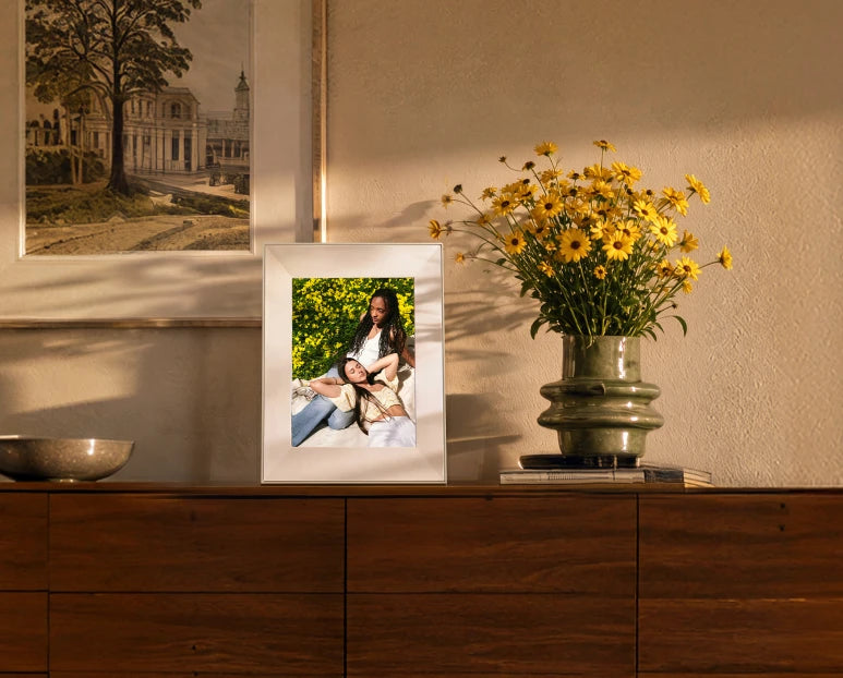 Frame on a sideboard beside a vase of yellow flowers